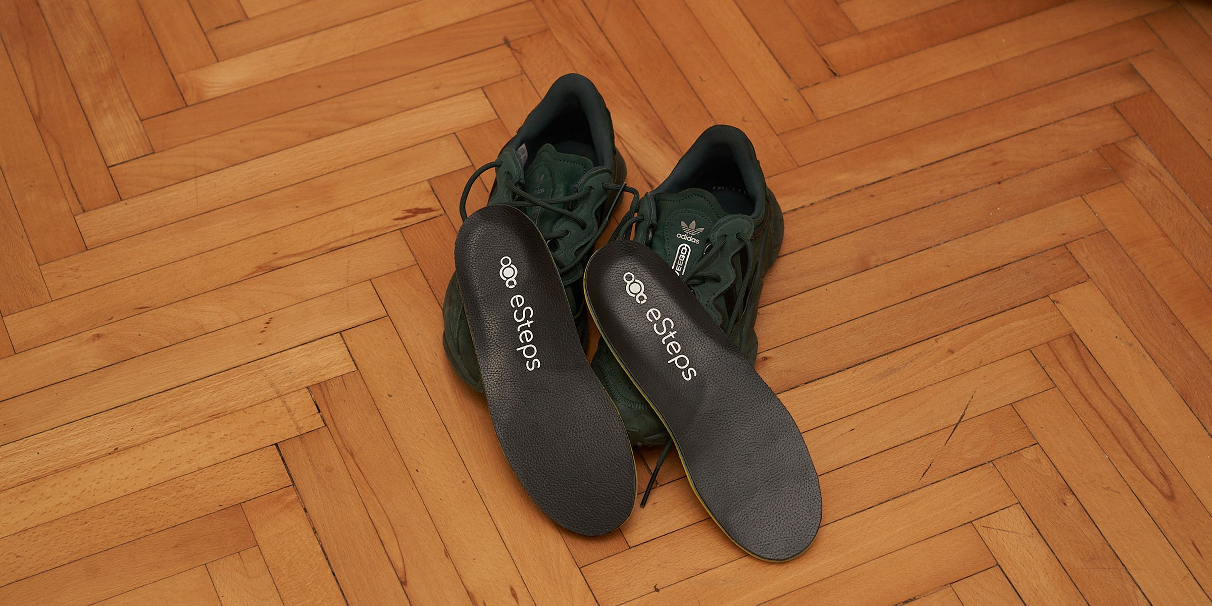 A pair of eSteps insoles resting on ordinary trainers on a wooden floor